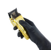 Gold hair clipper held by a gloved hand on a white background