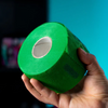 Hand holding a roll of green Rolda neck strips against a blue background
